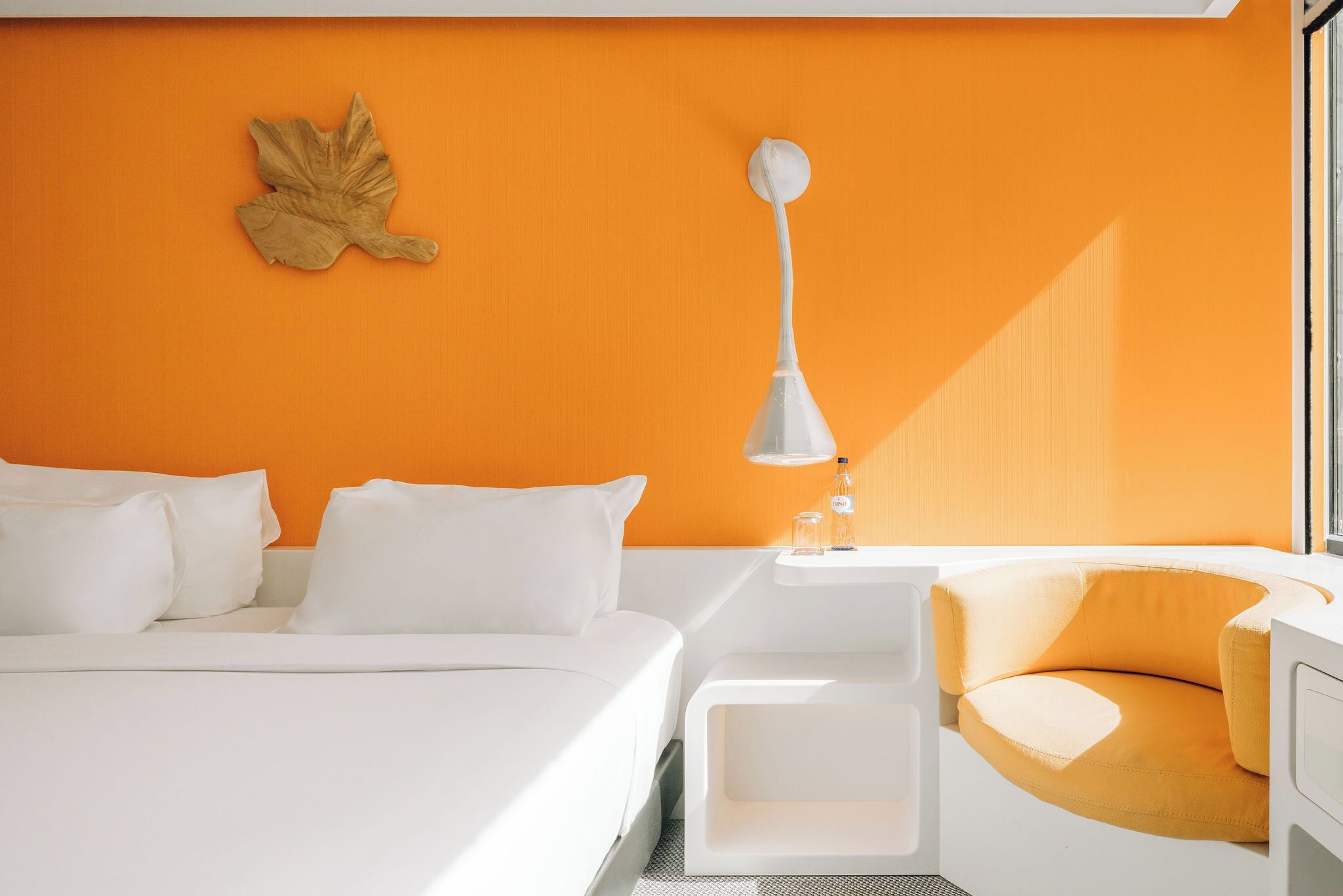 Une chambre d’hôtel moderne comprenant un lit, une table de chevet, une lampe et un coin salon aux lignes courbes.
