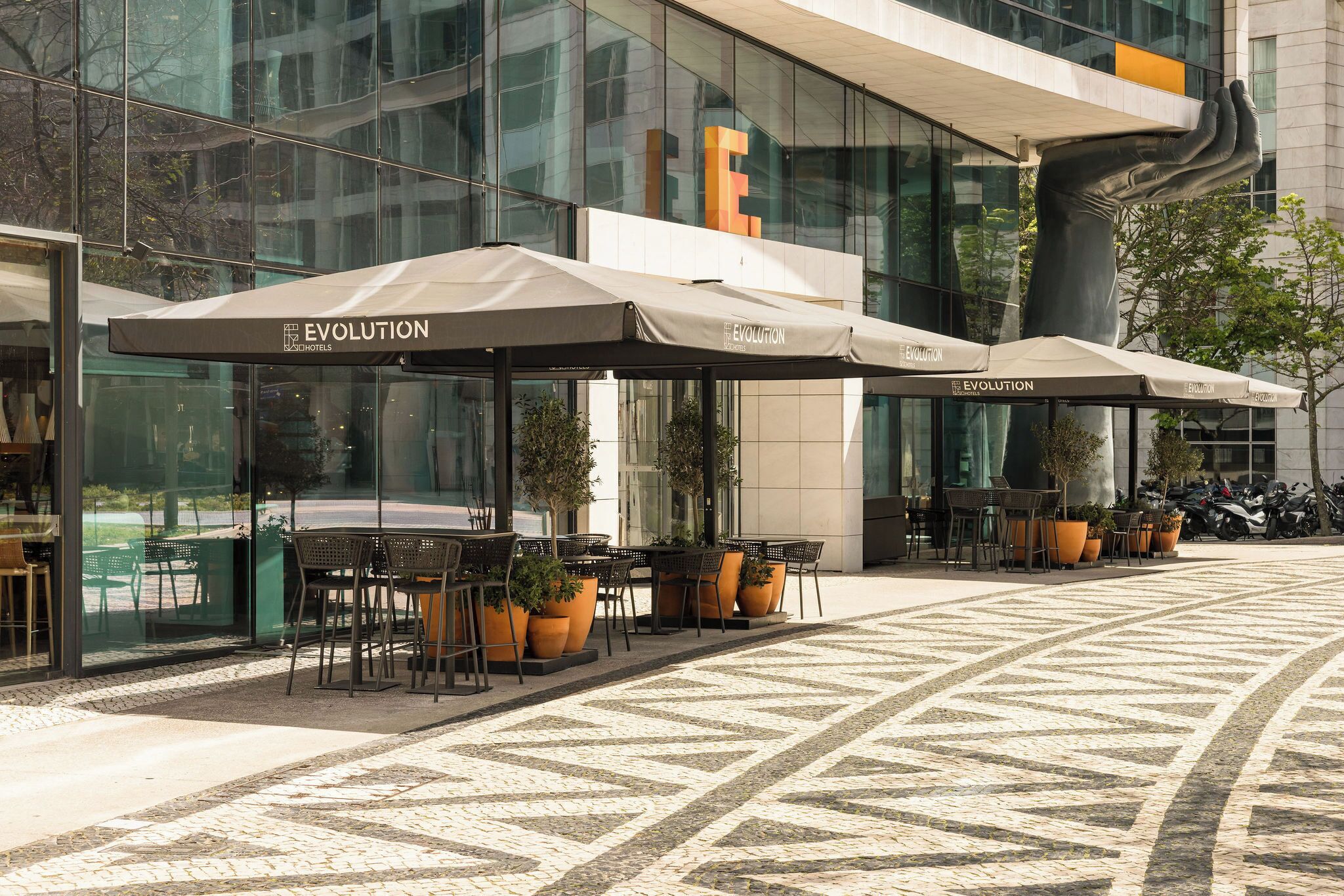 Outdoor seating with umbrellas, a modern building facade, and a patterned floor.