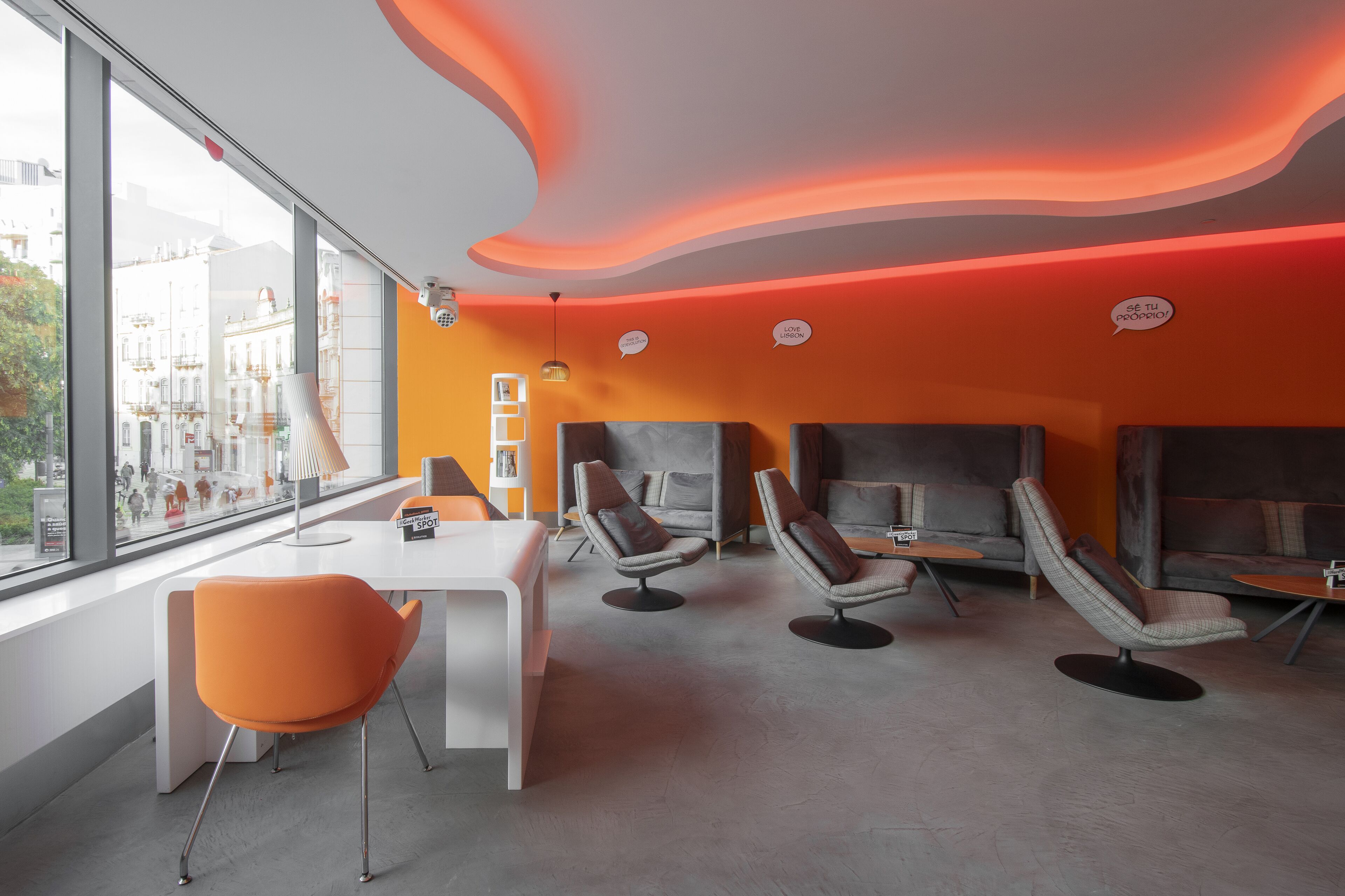 A modern lounge area with a white table, orange chairs, and grey sofas.