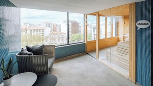 A modern room with a large window, a sofa, a small table, and a sauna area. - EVOLUTION Lisboa Hotel (Lisbon)