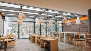 Un restaurante moderno con mesas y sillas de madera, lámparas colgantes y grandes ventanales con vistas.