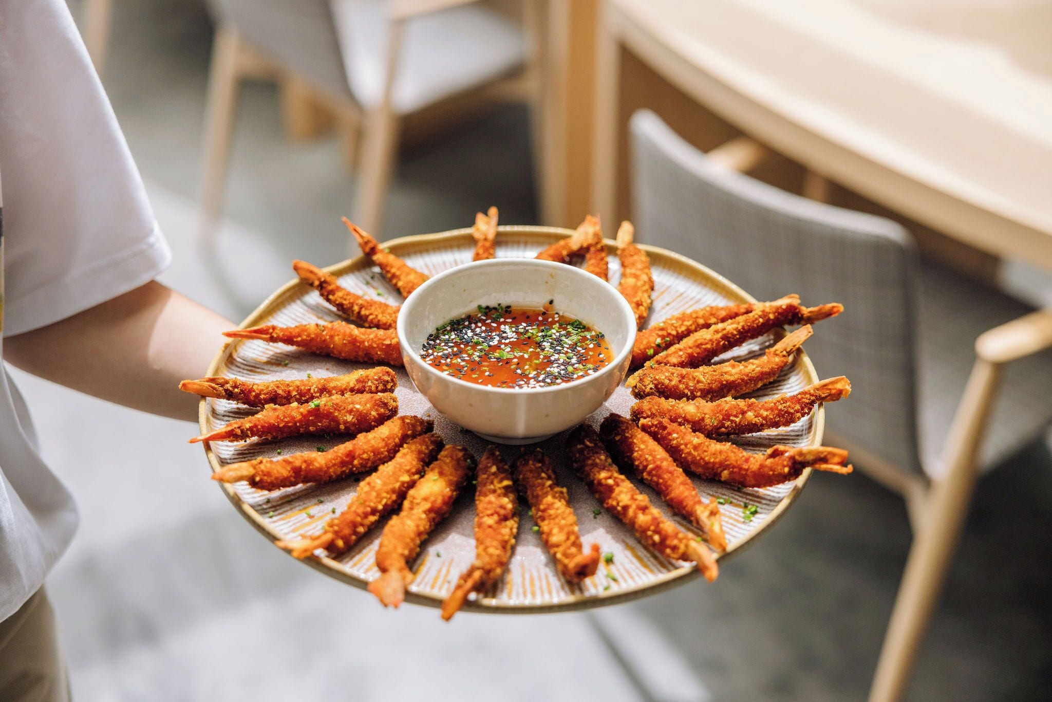 A person holding a tray with fried food and a dipping sauce.