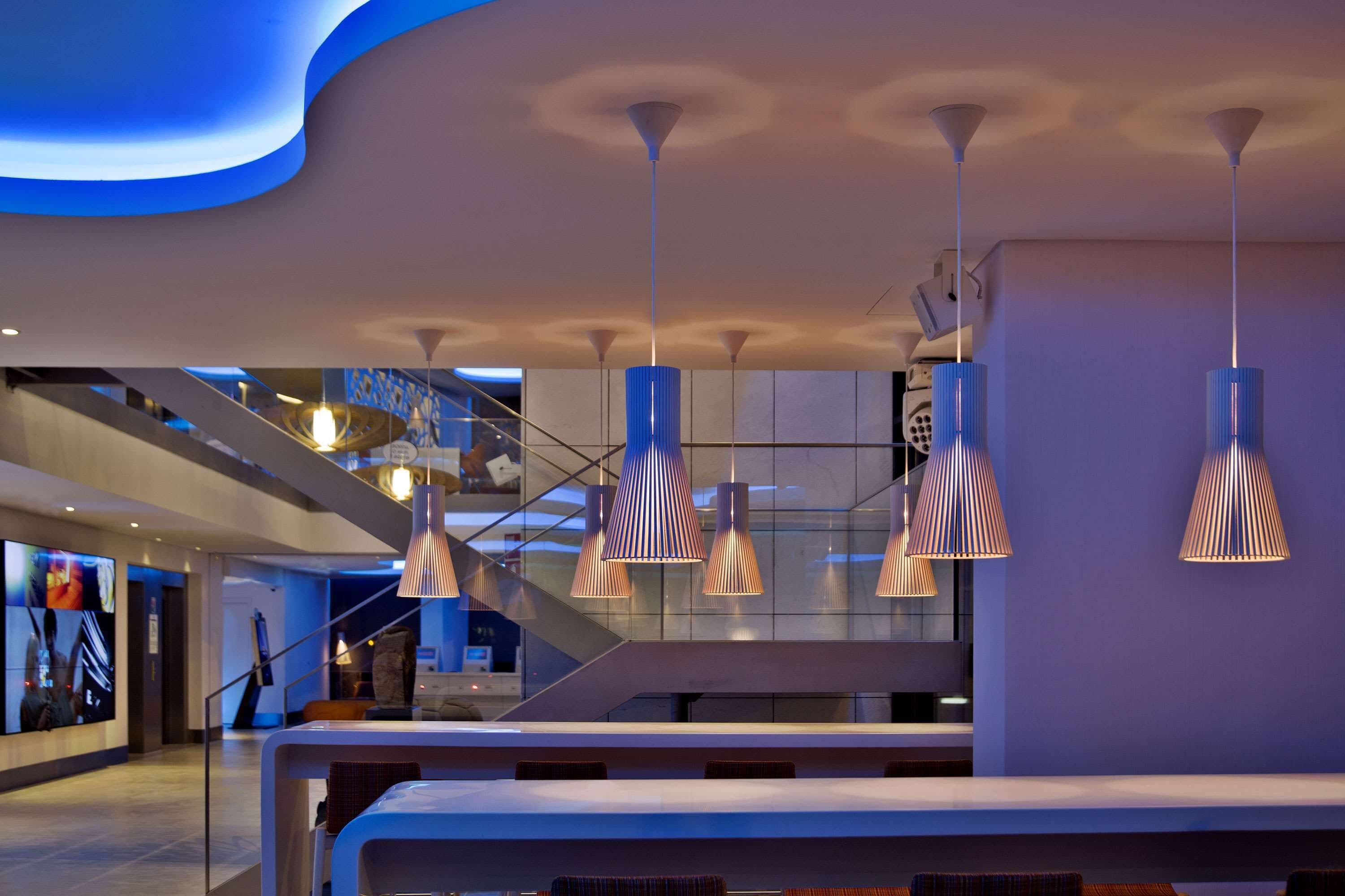 A modern hotel lobby with a spacious seating area, a staircase, and a large digital display wall.