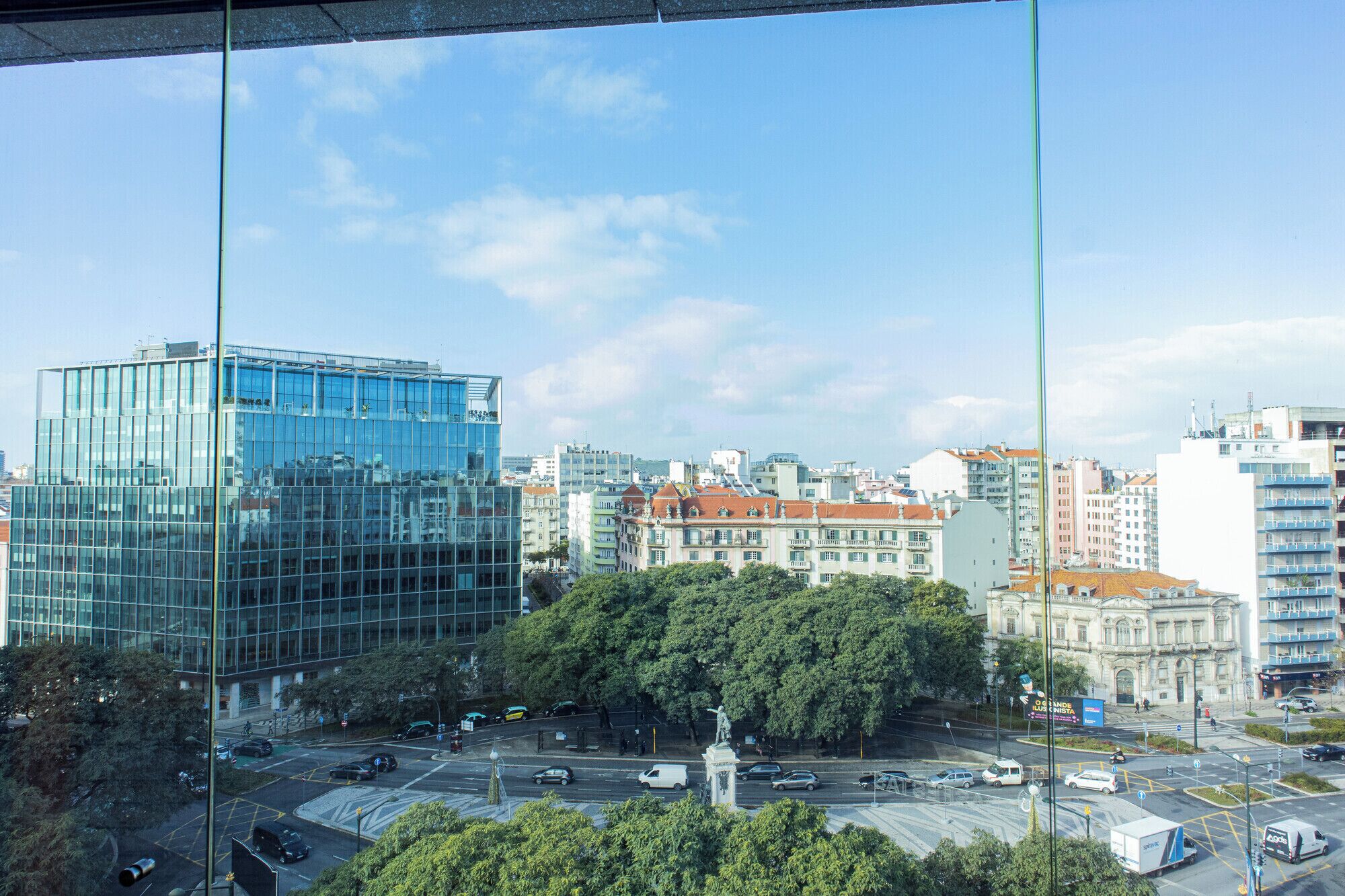 A cityscape with modern and historic buildings, a statue, and a busy intersection.