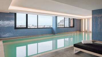 Una piscina interior moderna con vistas a la ciudad, un área de descanso con un banco y una pared de azulejos.
