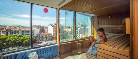 A modern spa room with a large window offering a city view, wooden benches, and a tiled floor.