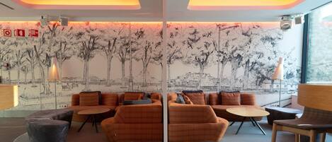 A modern lounge with orange sofas, a round coffee table, and a large window.