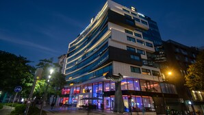 Un hotel moderno con varios pisos, amplias ventanas y un área de entrada destacada con asientos al aire libre.
