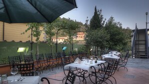 An outdoor patio with tables and chairs, a green wall, and a building in the background. - Hotel Italia Ristorante Pizzeria (Reggello)