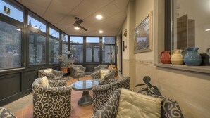 A sunroom with patterned sofas, a glass coffee table, and a ceiling fan. - Hotel Italia Ristorante Pizzeria (Reggello)