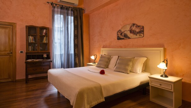 A bedroom with a large bed, bedside lamps, a nightstand, a wooden dresser, and a bookshelf. - Navona Tower Relais (Rome)