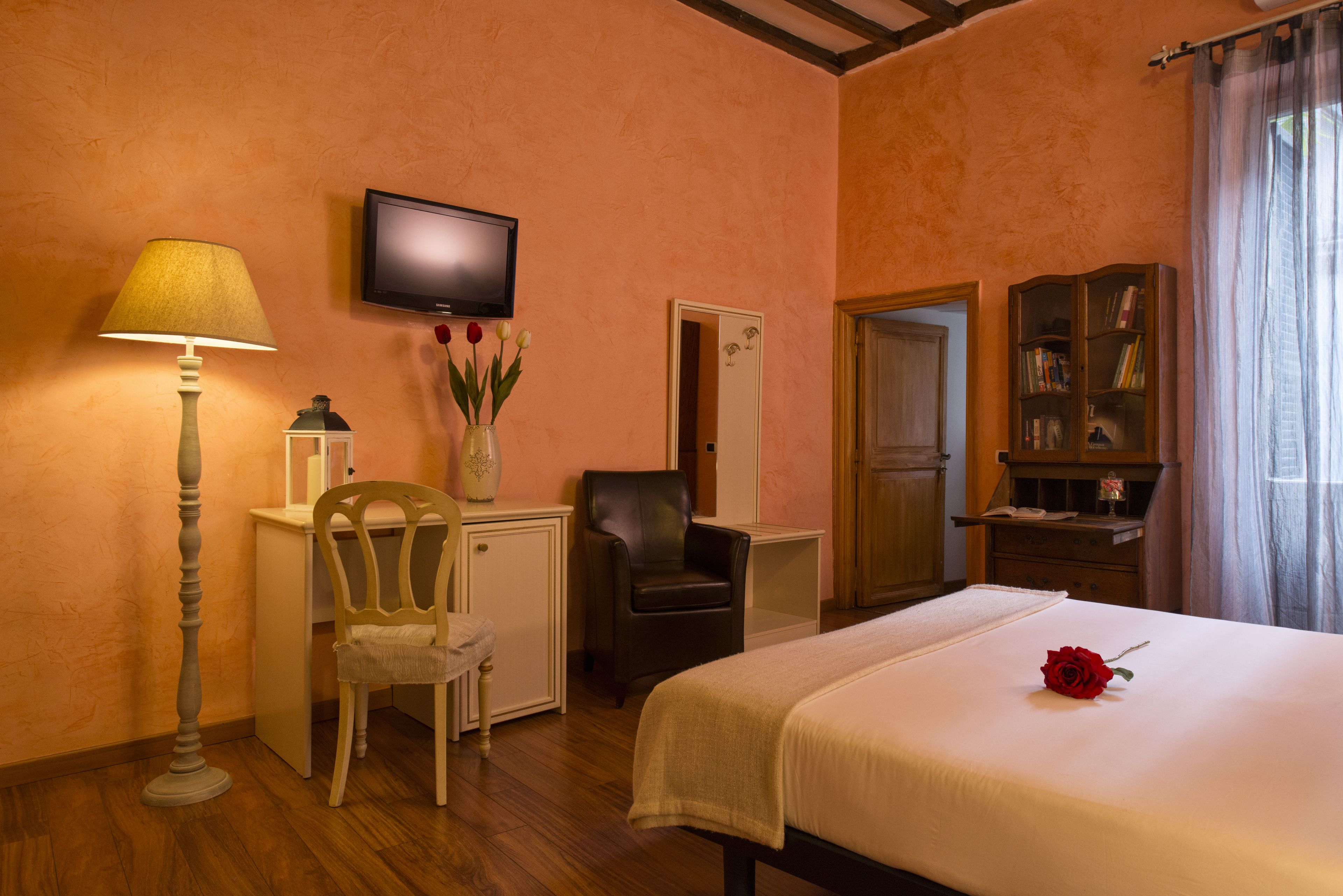 A hotel room with a bed, a desk, a chair, a television, and a bookshelf.