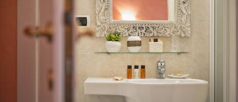 A bathroom with a white sink, a mirror with an ornate frame, and a glass shelf holding toiletries.