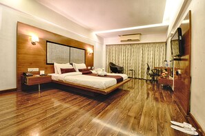 Ein modernes Hotelzimmer mit einem großen Bett, Holzboden, einem Schreibtisch mit Stuhl, einem Fernseher und einem Badezimmer mit Dusche und Toilette.
