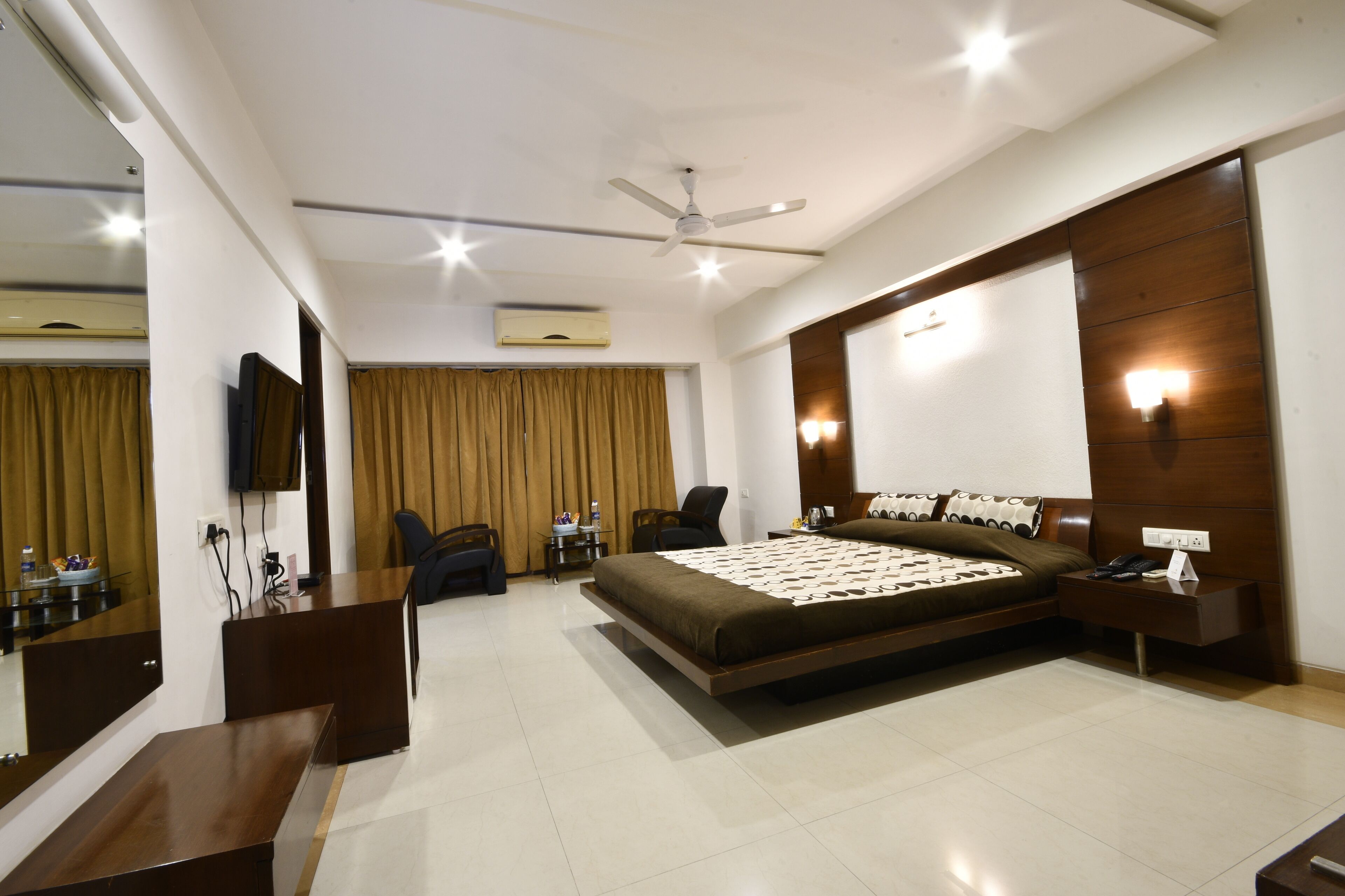 A modern hotel room with a bed, a desk, a chair, a TV, and a ceiling fan.