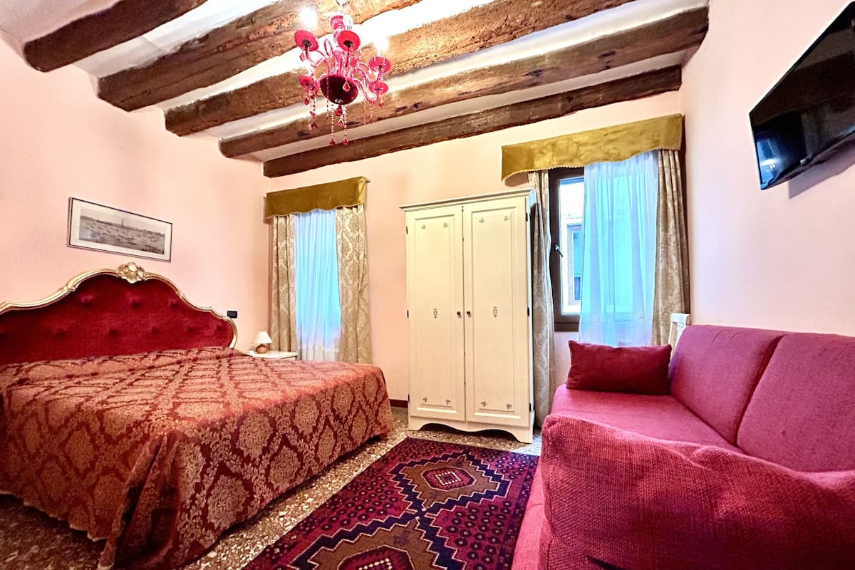 A bedroom with a large bed, a red sofa, a wardrobe, and a chandelier.