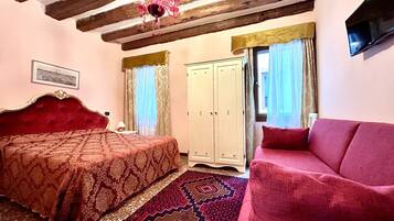 A bedroom with a large bed, a red sofa, a wardrobe, and a chandelier.