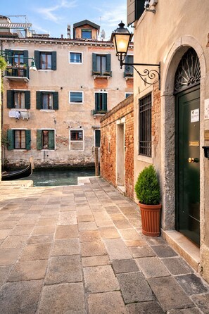 A narrow Venetian alley with stone paving, a canal, and traditional buildings with balconies and shutters. - Alloggi Serena (Venice)