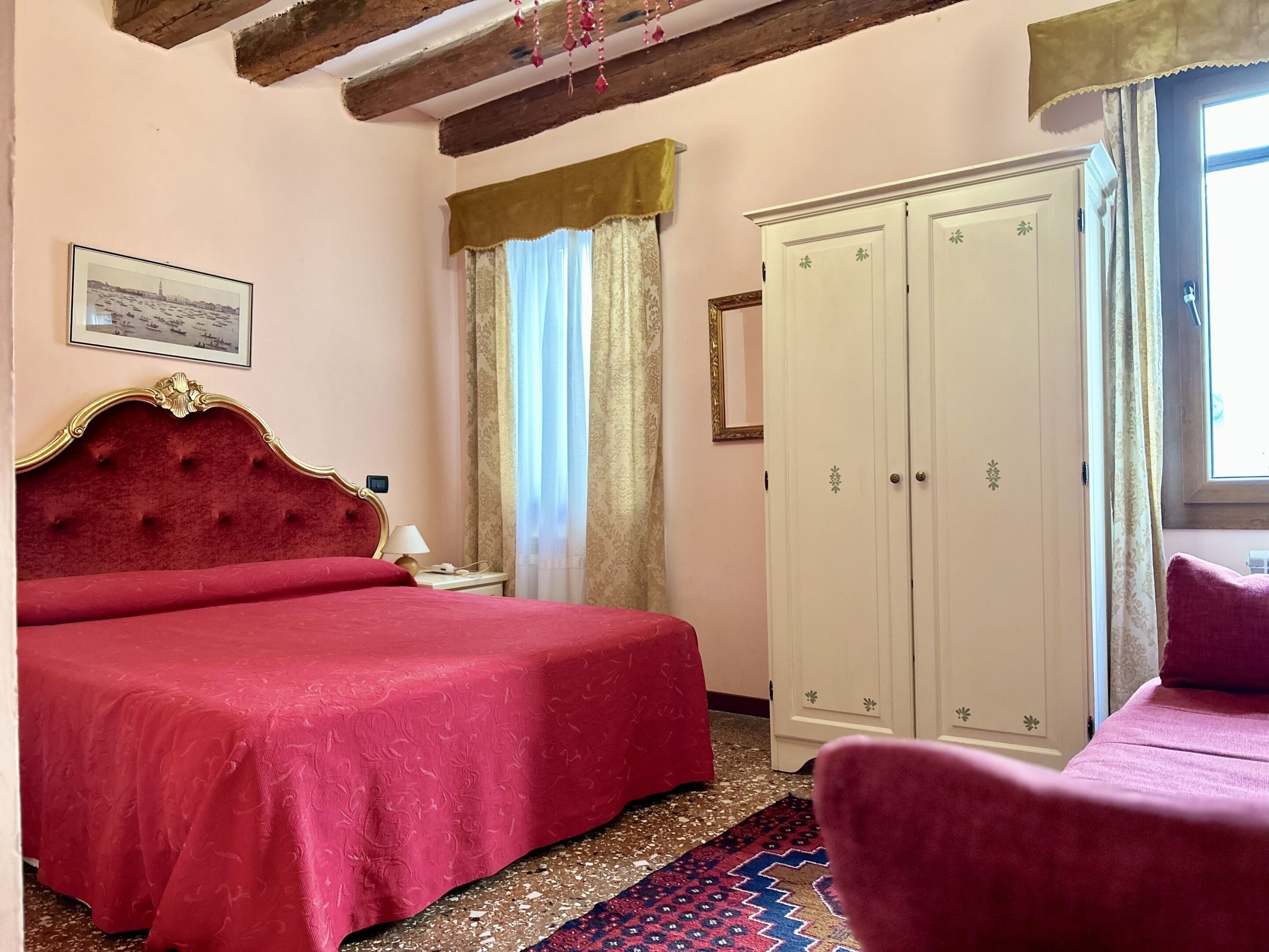 A bedroom with a large bed, a wardrobe, a chair, and a window with curtains.