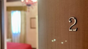 A hotel room with a wooden door marked with the number 2, a red bedspread, and a chandelier in the background. - Alloggi Serena (Venice)