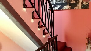 A staircase with a black metal railing, a red carpeted landing, and a wall-mounted picture of boats. - Alloggi Serena (Venice)