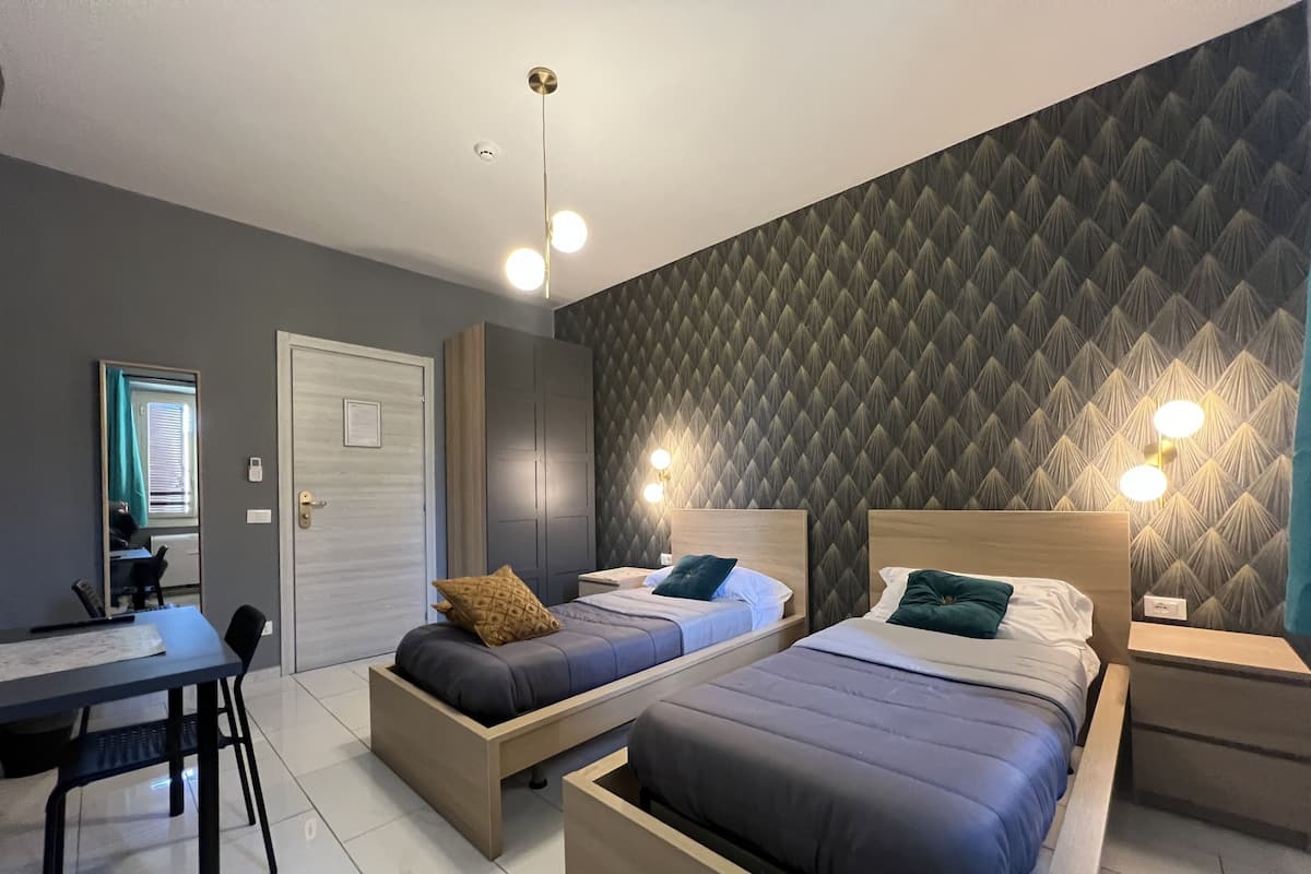 A modern bedroom with two beds, a desk, and a chair.