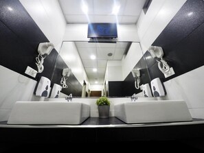 A modern bathroom with dual sinks, a large mirror, and a mounted television.