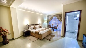 Ein Hotelzimmer mit einem großen Bett, einem Nachttisch, einem Sessel, einem kleinen Tisch mit einer Vase und Blick ins Badezimmer.