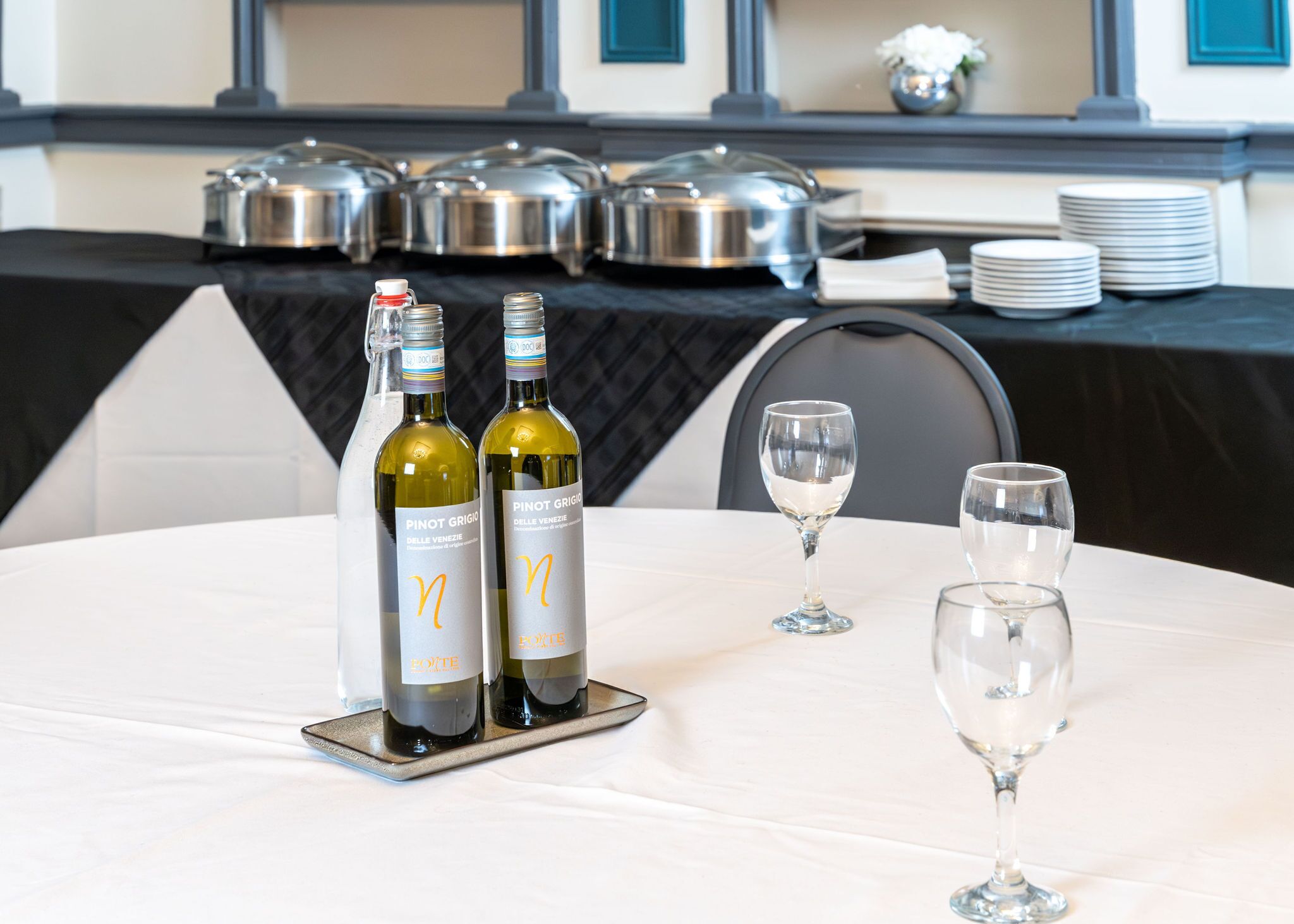 Una mesa con dos botellas de vino Pinot Grigio y dos copas de vino vacías.