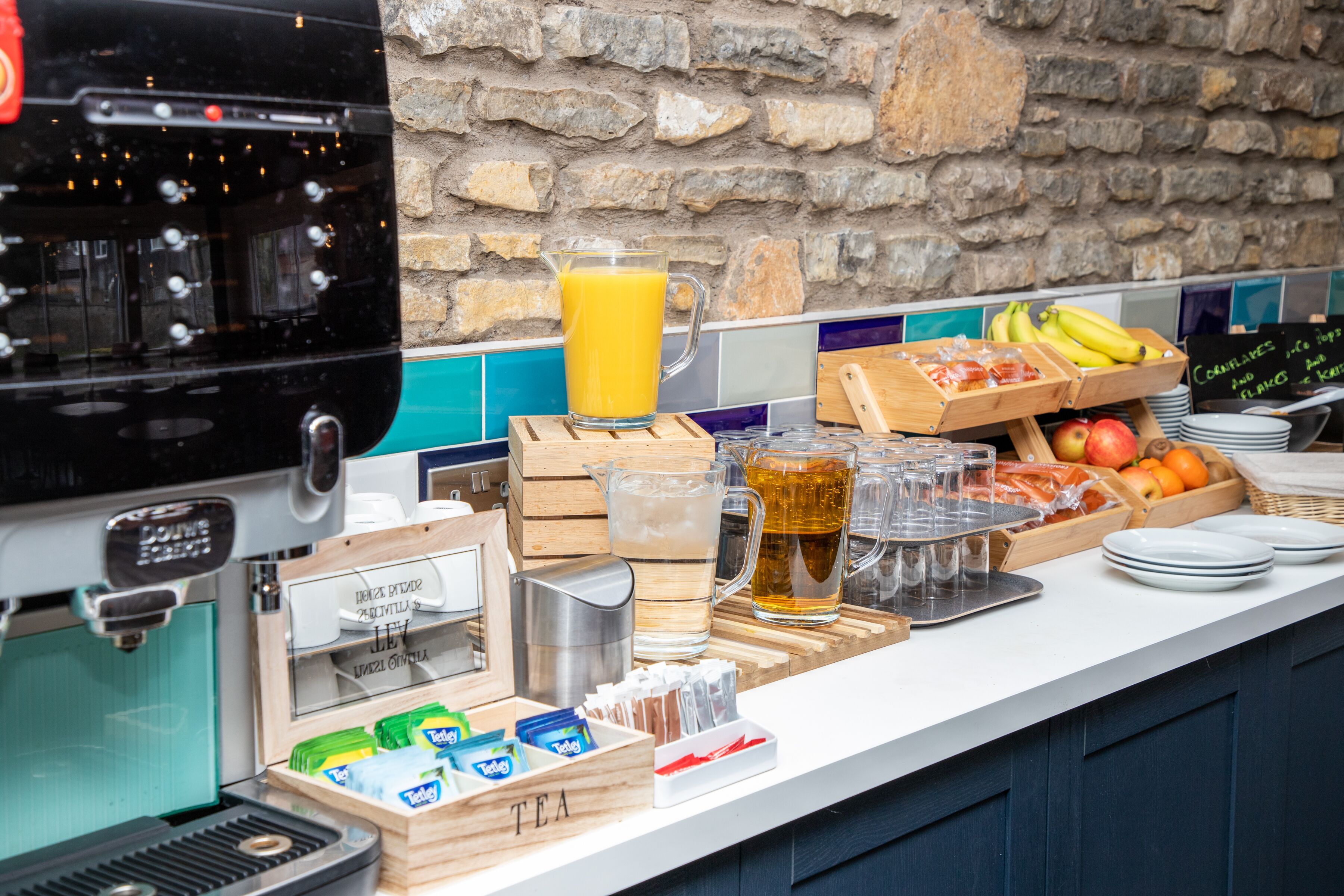 A breakfast bar with a coffee machine, tea, juice, and fruits.