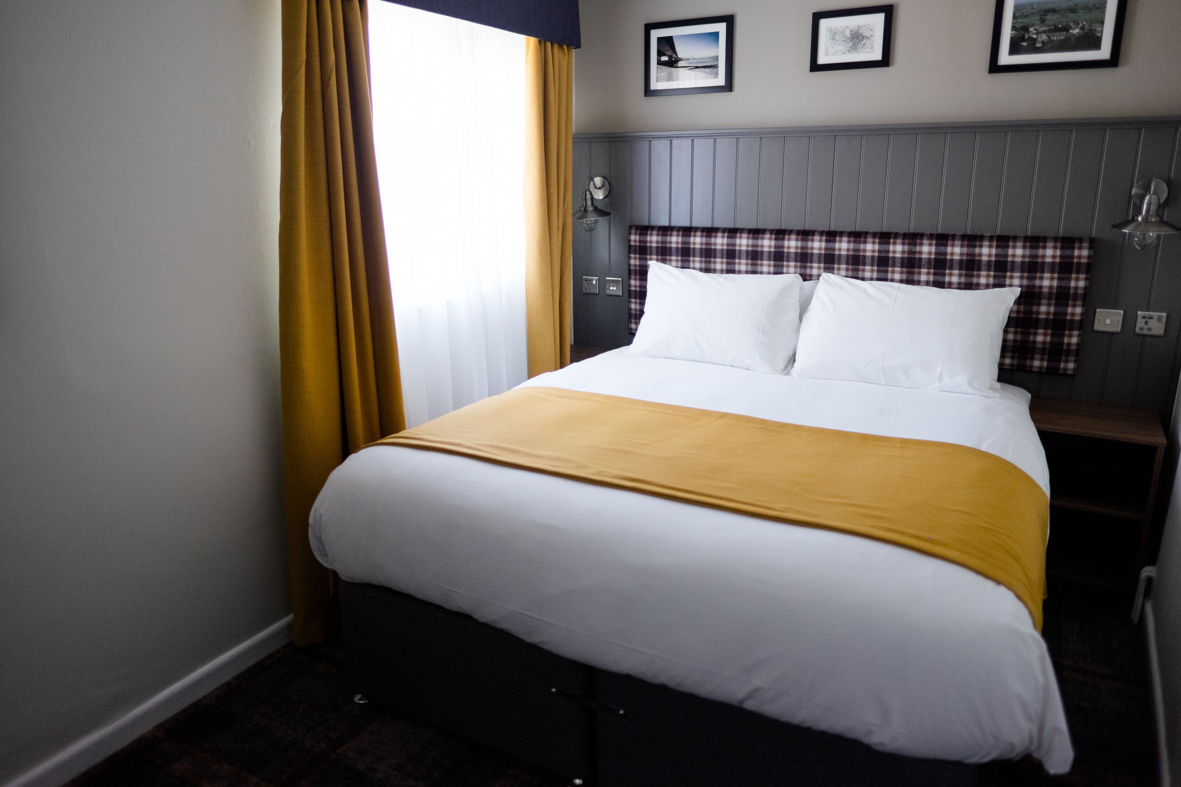 Une chambre d’hôtel avec un lit, une table de chevet, une lampe et une fenêtre avec des rideaux.