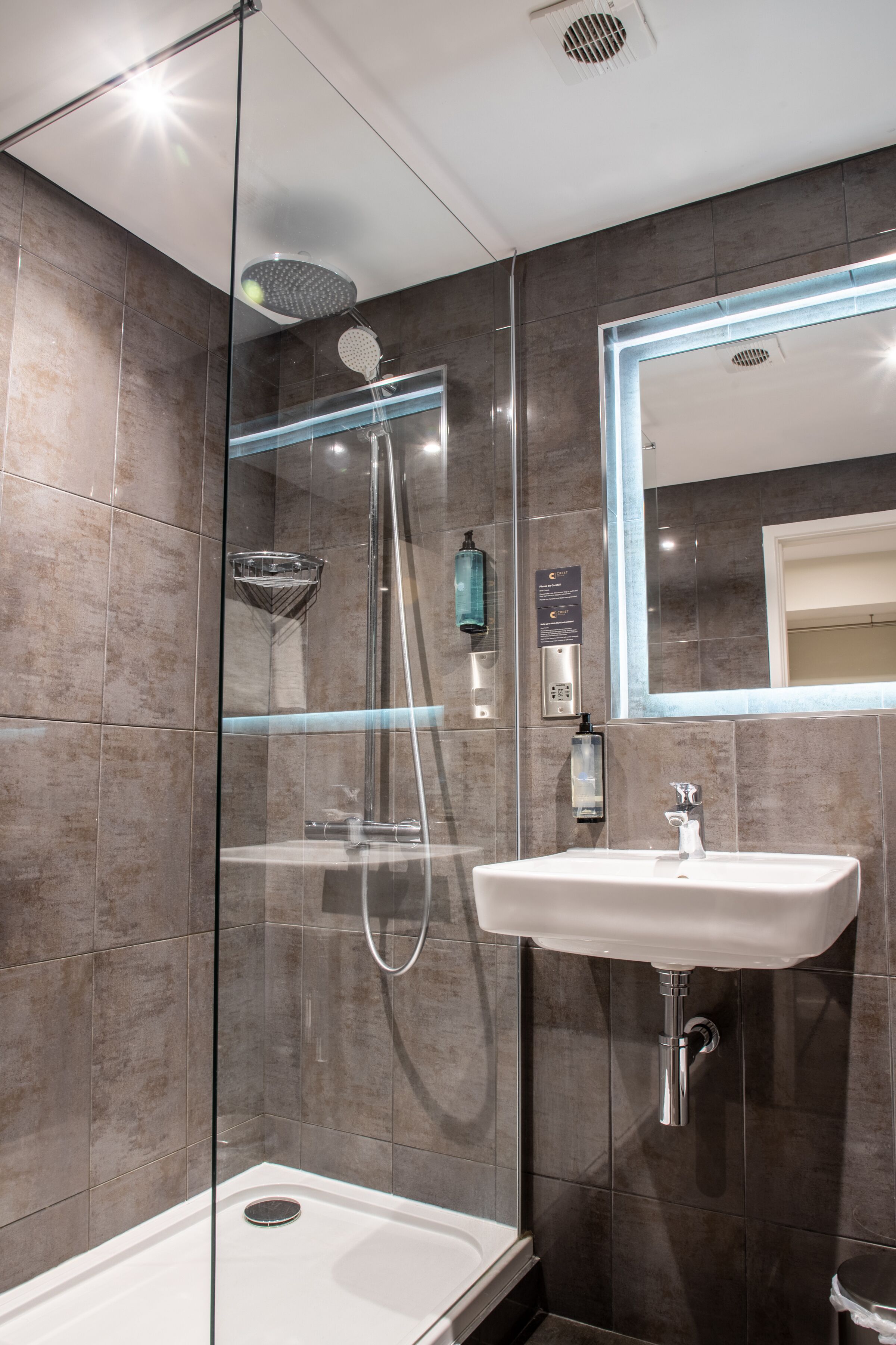A modern bathroom with a glass-enclosed shower, a white sink, and a mirror with LED lighting.