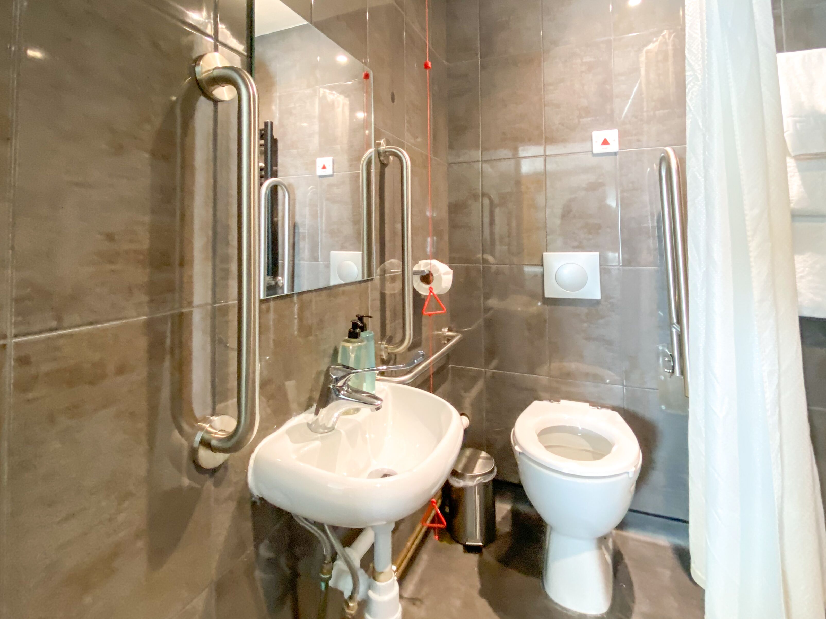 Un baño moderno con lavamanos, inodoro y barras de apoyo.