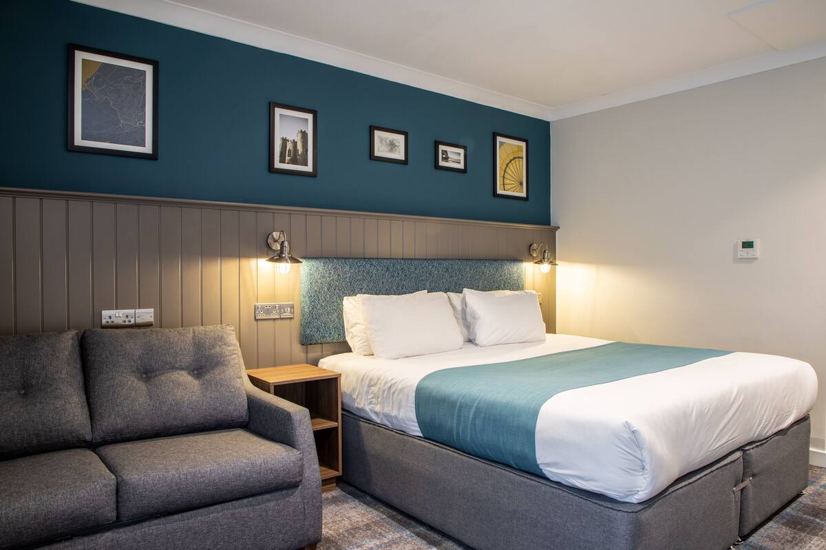 Quarto de hotel com cama, sofá e mesa de cabeceira com abajur.