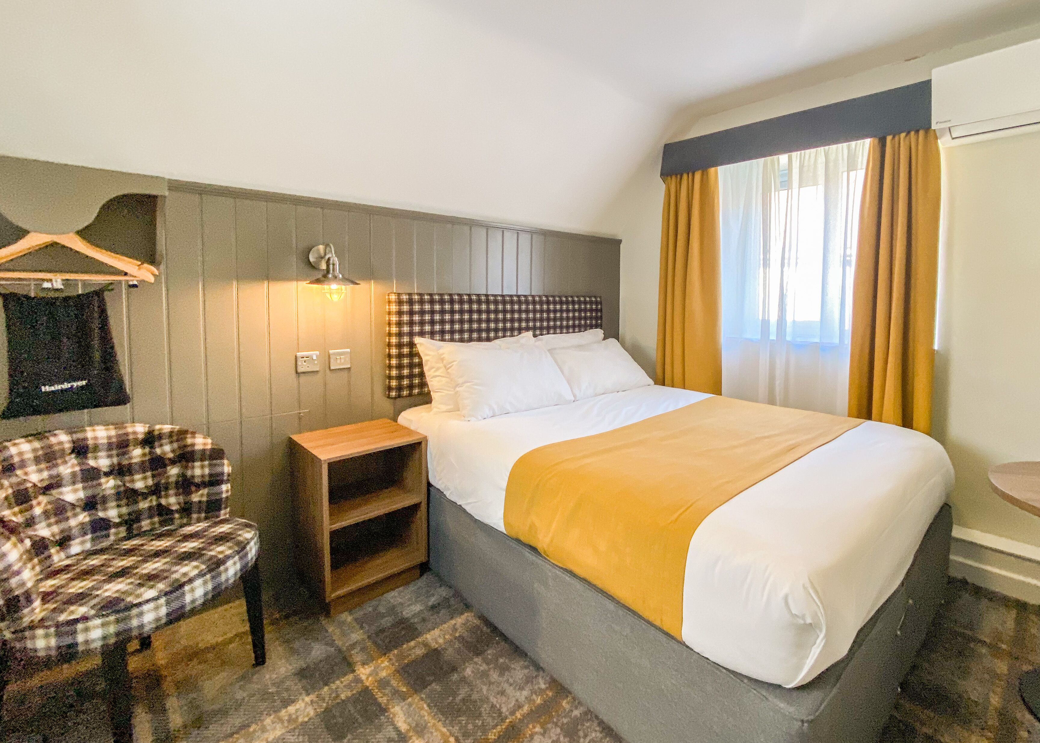 Una habitación de hotel con cama, una silla, una mesita de noche y una lámpara fijada a la pared.