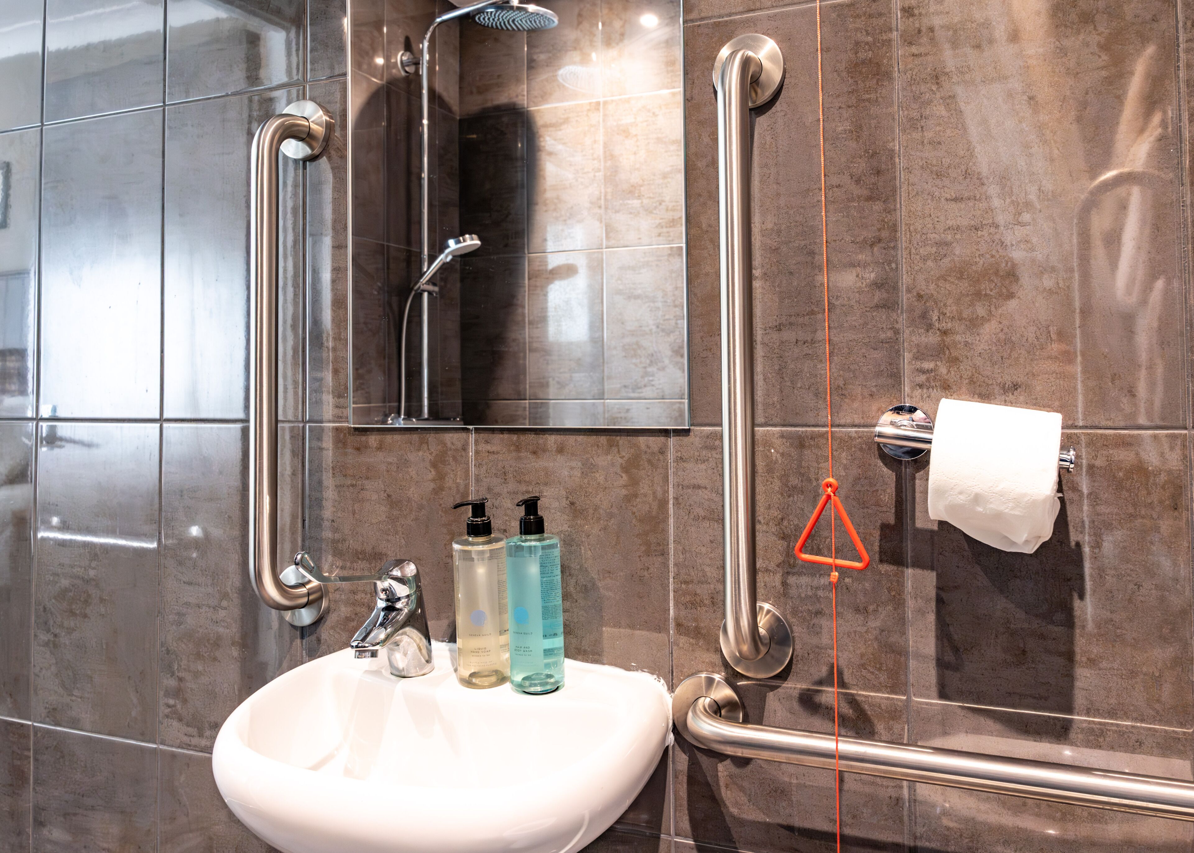 Une salle de bain avec un lavabo blanc, deux flacons de savon liquide, un miroir et un porte-serviettes.