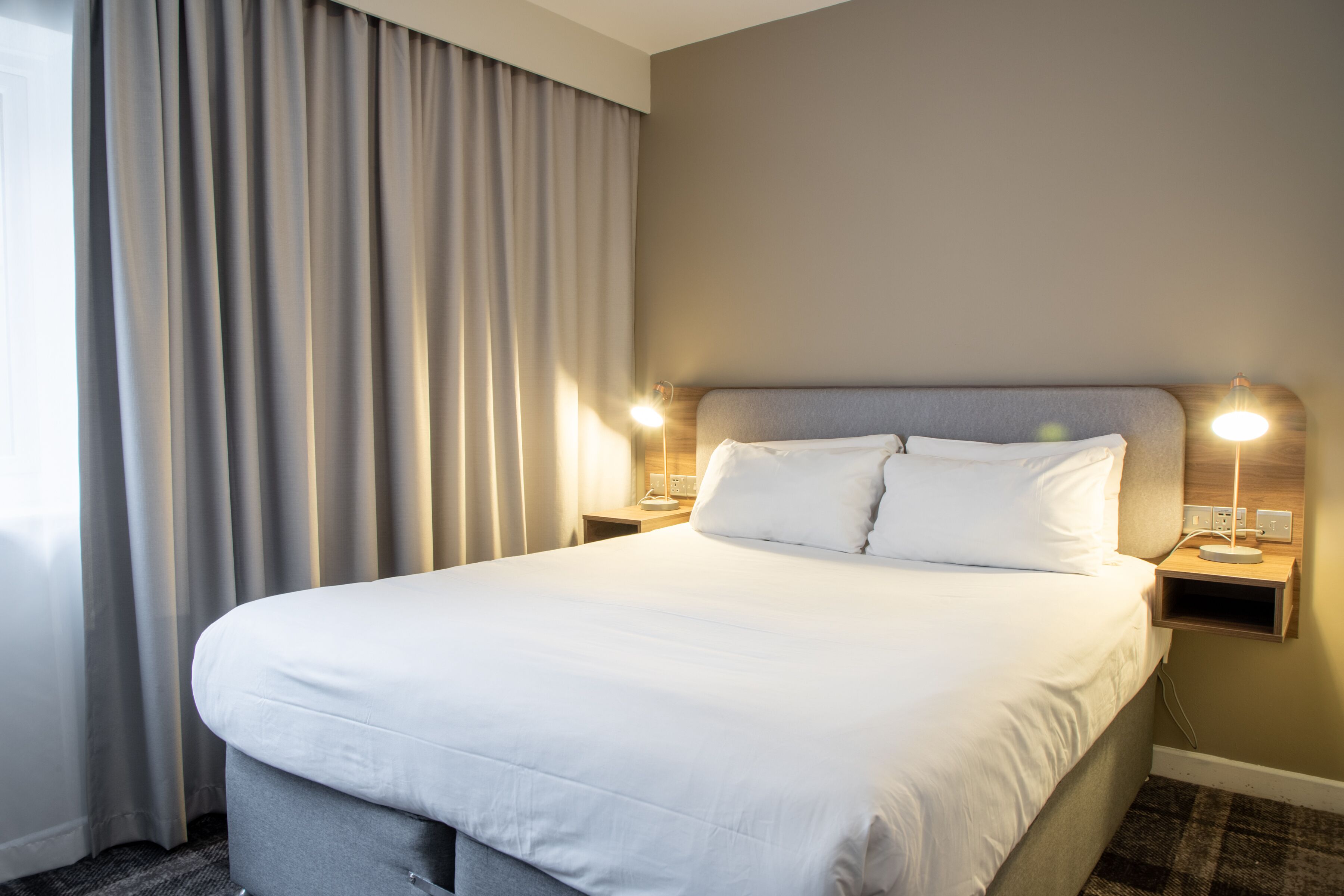 A hotel room with a large bed, two bedside tables with lamps, and a window with curtains.