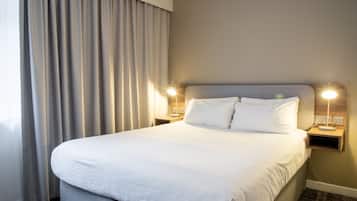 Una habitación de hotel con una cama grande, dos mesitas de noche con lámparas y un ventanal con cortinas.