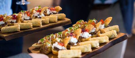 Una tabla de madera con diversos aperitivos, incluyendo rollitos de primavera y otras preparaciones pequeñas, probablemente servidos en un evento social o reunión.