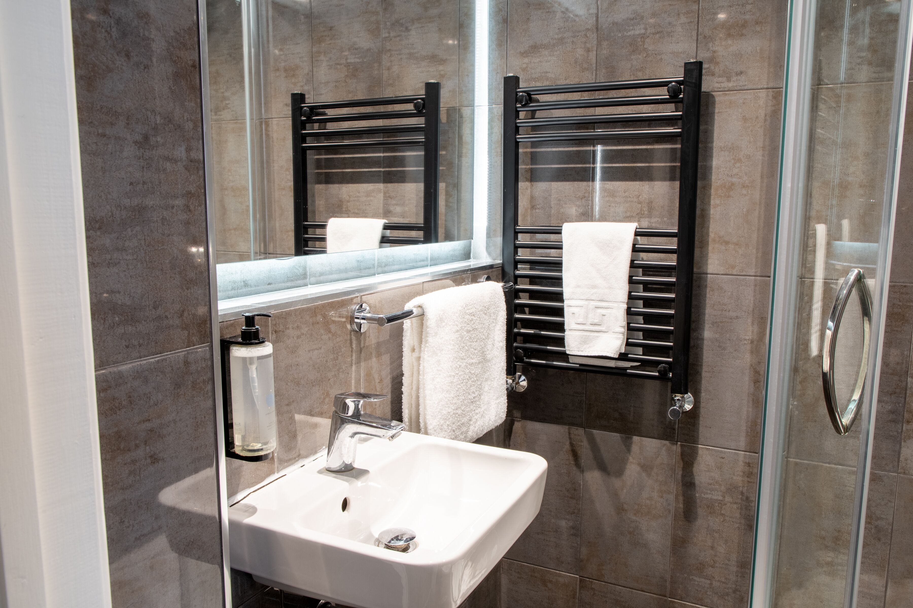 A modern bathroom with a glass shower enclosure, a white sink, and a towel rack.