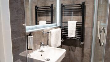 A modern bathroom with a glass shower enclosure, a white sink, and a towel rack.