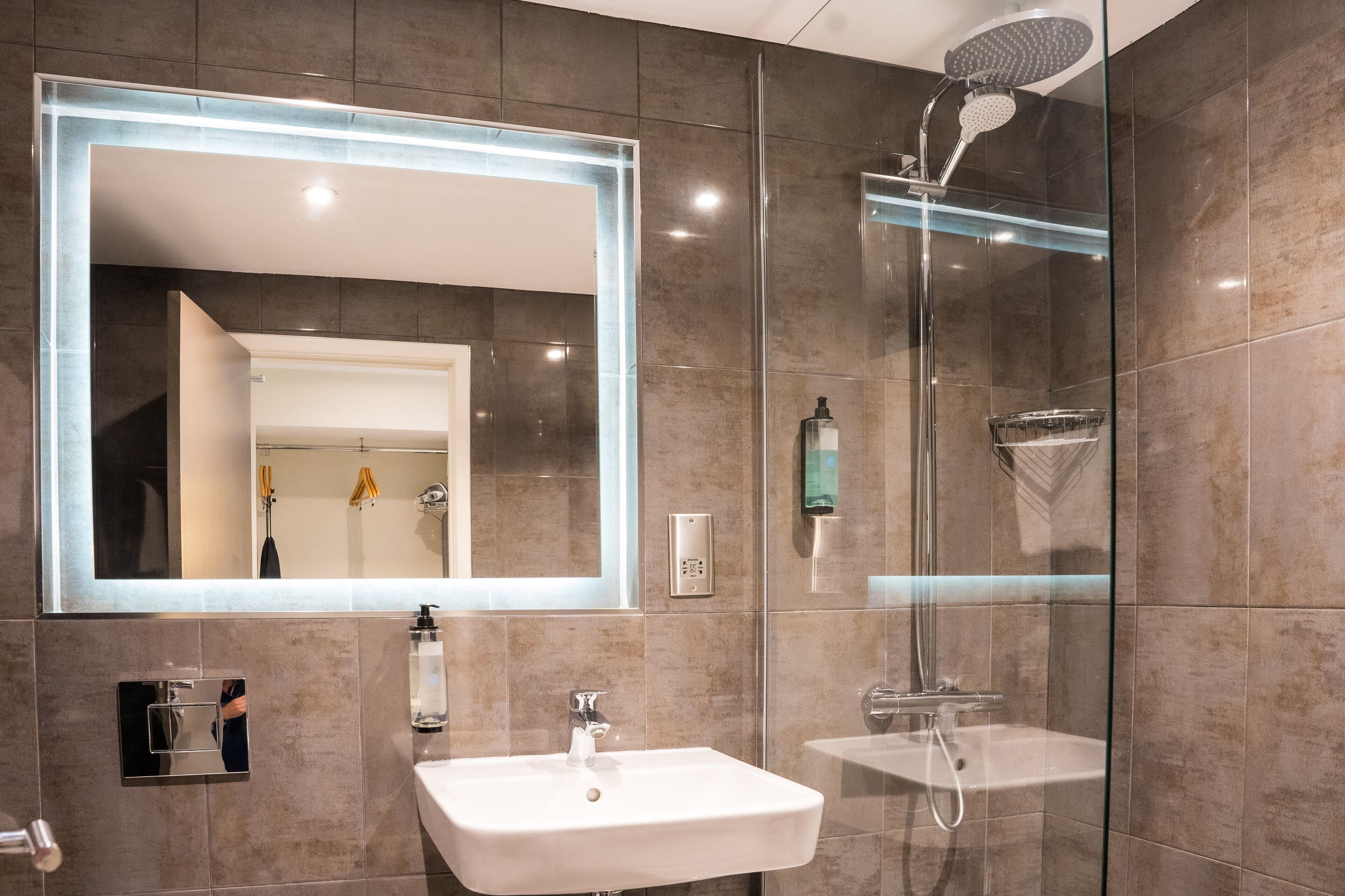 Un baño moderno con un espejo grande, dos lavamanos, una ducha y zona de ducha con mampara de vidrio.