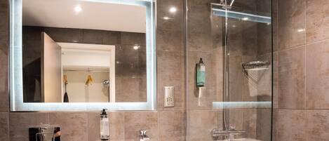 Un baño moderno con un espejo grande, dos lavamanos, una ducha y zona de ducha con mampara de vidrio.