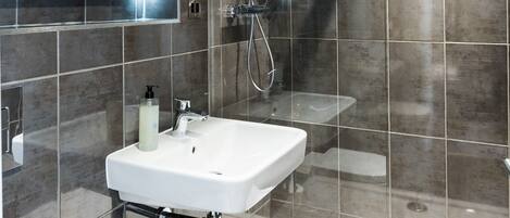 A modern bathroom with a white sink, a handheld showerhead, and a glass shower enclosure.