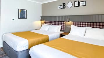 Habitación de hotel con dos camas, cada una con ropa de cama blanca y una manta color mostaza. Hay luces empotradas en la pared y un cuadro enmarcado sobre las camas.