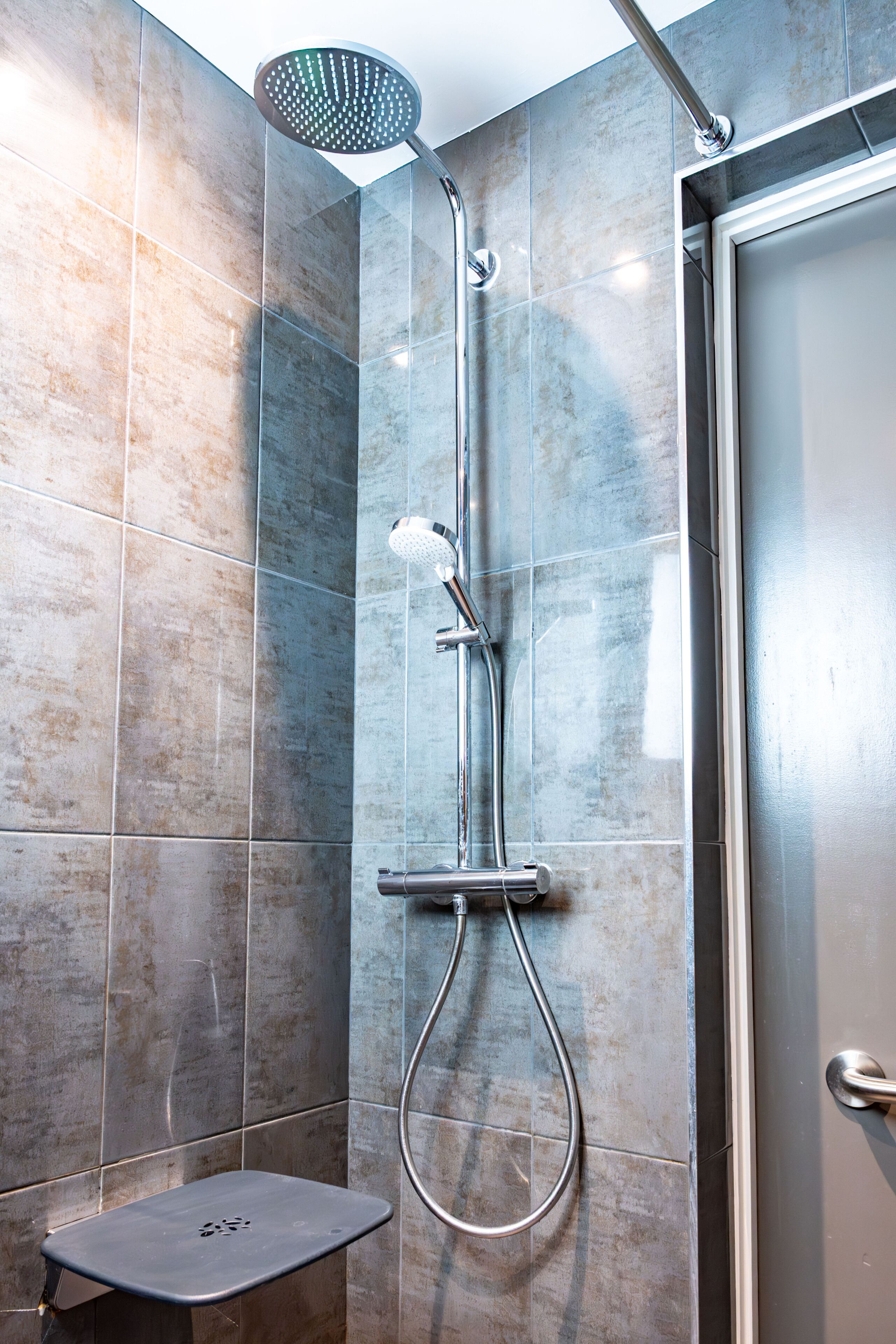 A modern shower with a handheld showerhead and a wall-mounted faucet.