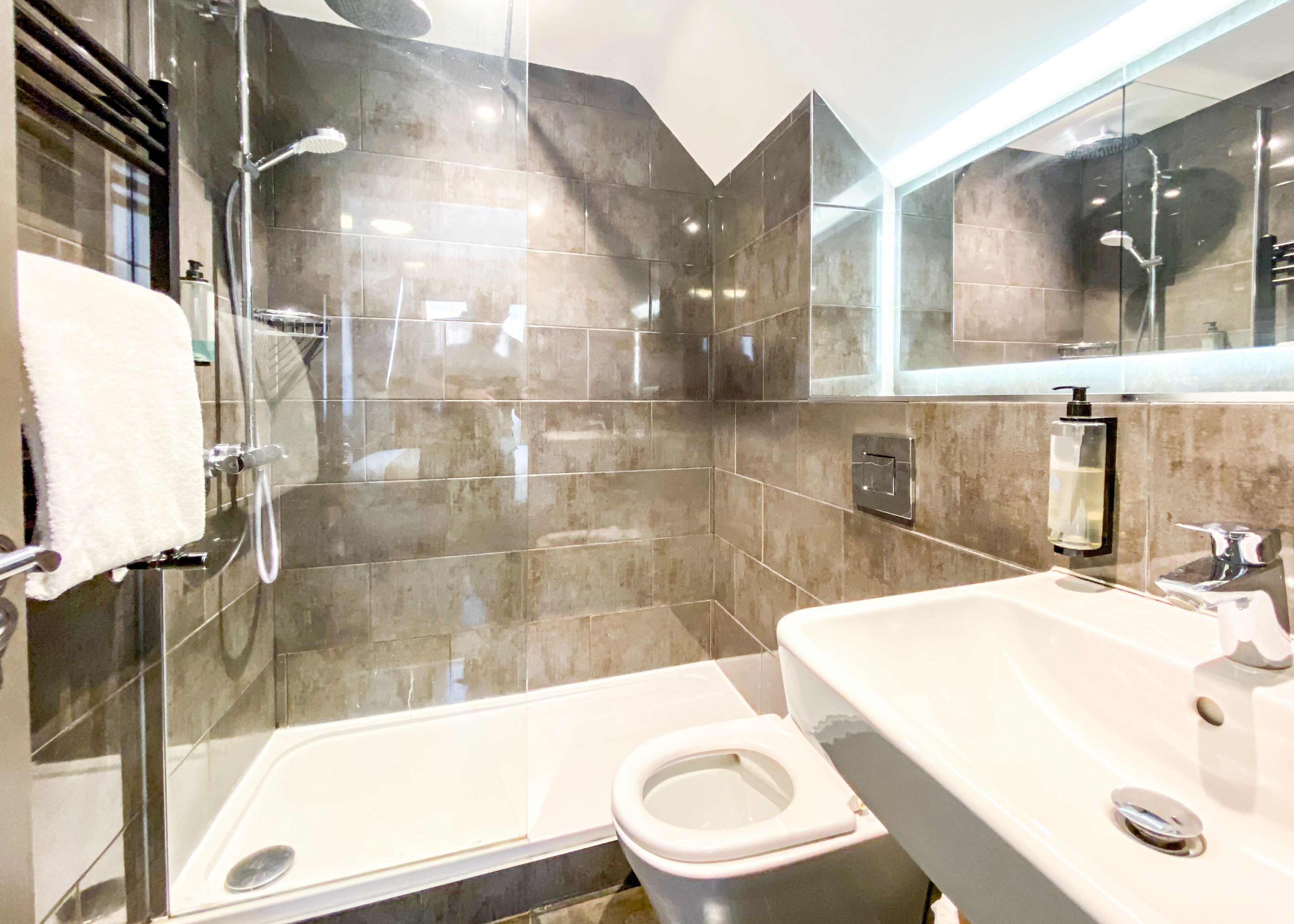 A modern bathroom with a glass-enclosed shower, a white bathtub, and a sink with a mirror above it.