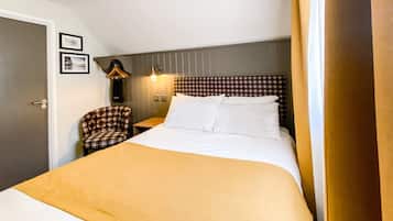 Et hotelværelse med en seng, en stol, et natbord og en lampe.