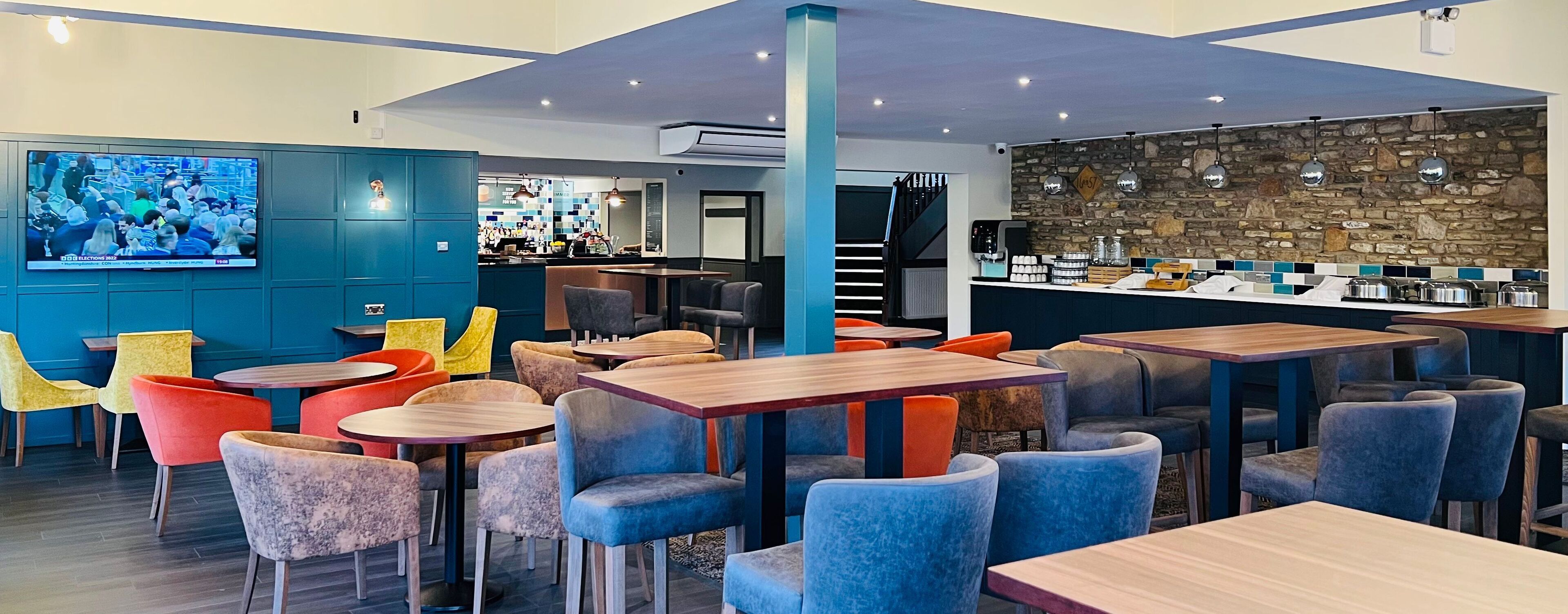 A modern restaurant with a bar area, multiple seating options including tables and chairs, and a stone accent wall.