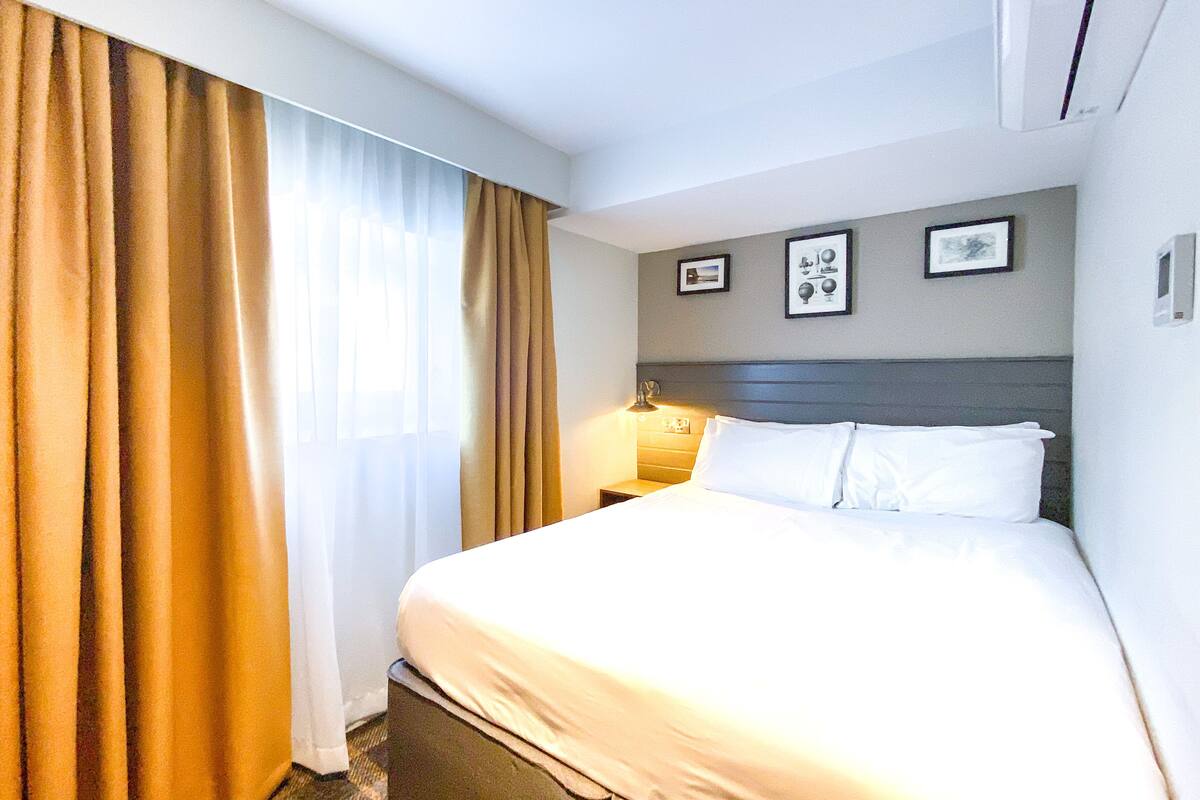 Quarto de hotel com cama, cortinas, mesa de cabeceira e quadros pendurados na parede.
